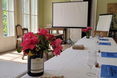 Salle en pierre avec de grandes tables dressées, éclairée par des lustres faits de bouteilles en verre vert.