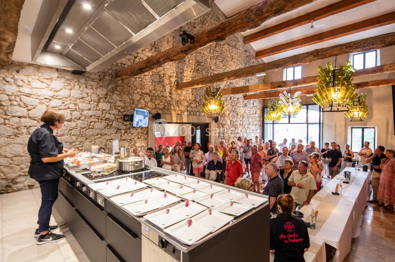 Démonstration culinaire devant un public dans une salle en pierre avec poutres apparentes et éclairage moderne.