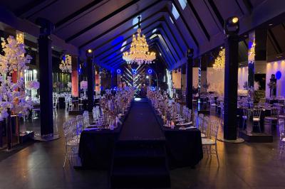 Salle de réception élégante avec tables rondes dressées, chaises transparentes et lustres suspendus.
