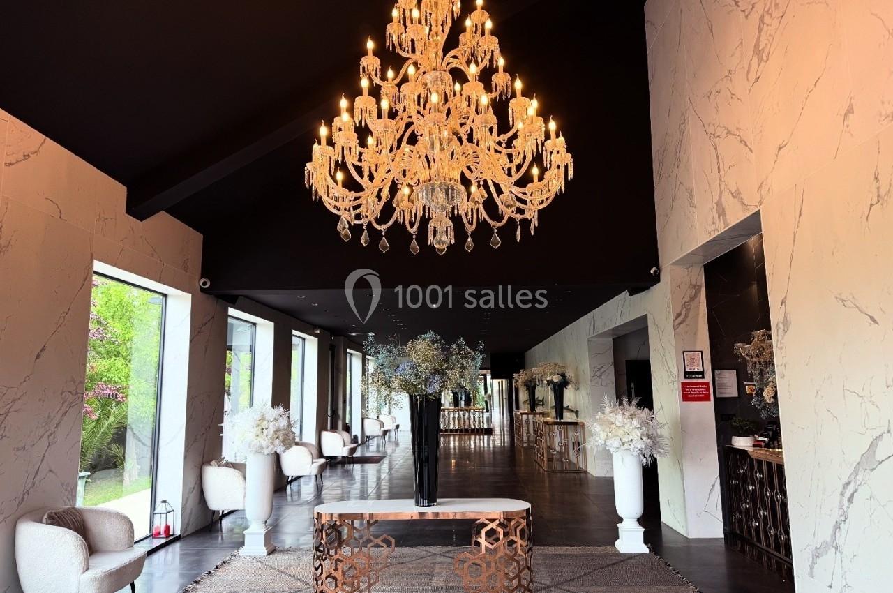 Hall d'entrée élégant avec un grand lustre, des murs en marbre, des fauteuils et des arrangements floraux.