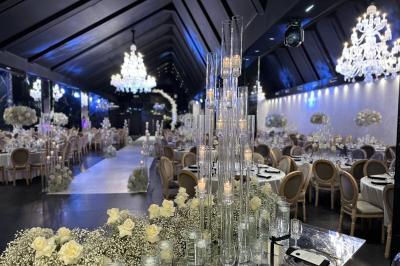 Salle de réception élégante avec tables rondes dressées, chaises transparentes et lustres suspendus.