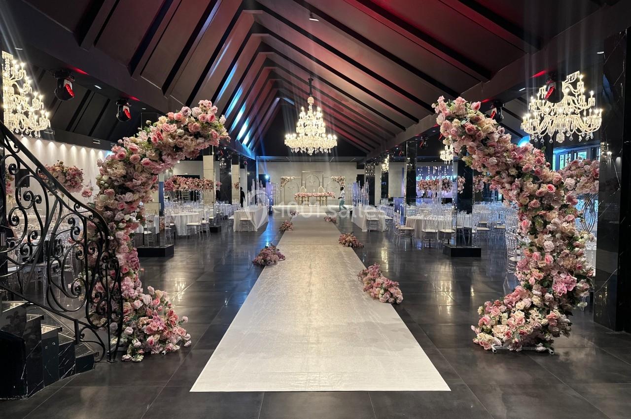 Salle de réception élégante avec allée centrale bordée d'arcs fleuris et lustres suspendus.