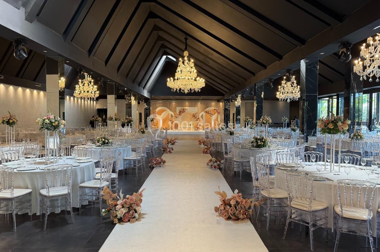 Salle de réception élégante avec tables dressées, chaises transparentes, chandeliers et allée décorée de fleurs.