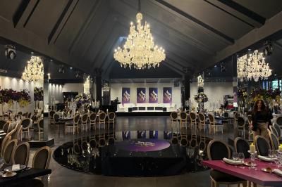 Salle de réception élégante avec tables rondes dressées, chaises transparentes et lustres suspendus.