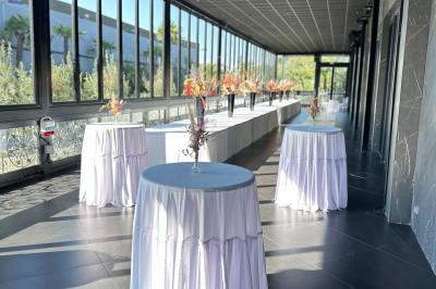 Salle de réception élégante avec tables rondes dressées, chaises transparentes et lustres suspendus.