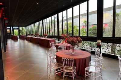 Salle de réception élégante avec tables rondes dressées, chaises transparentes et lustres suspendus.