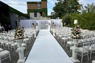 Salle de réception élégante avec tables rondes dressées, chaises transparentes et lustres suspendus.
