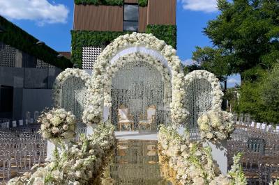 Salle de réception élégante avec tables rondes dressées, chaises transparentes et lustres suspendus.