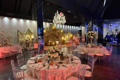Salle de réception élégante avec tables rondes dressées, chaises transparentes et lustres suspendus.