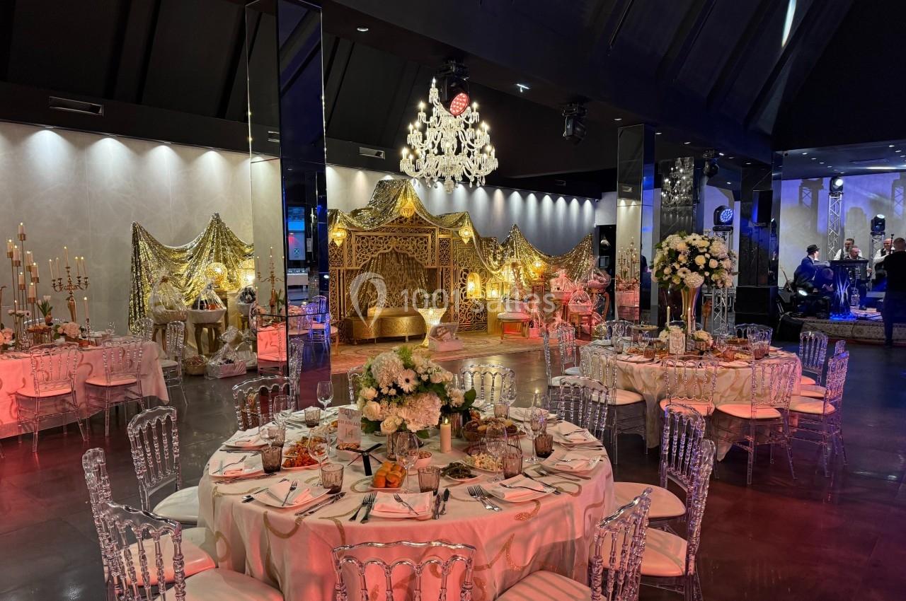 Salle de réception décorée avec des tables élégantes, des chaises transparentes et un espace orné de rideaux dorés.