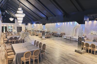 Salle de réception élégante avec tables rondes dressées, chaises transparentes et lustres suspendus.
