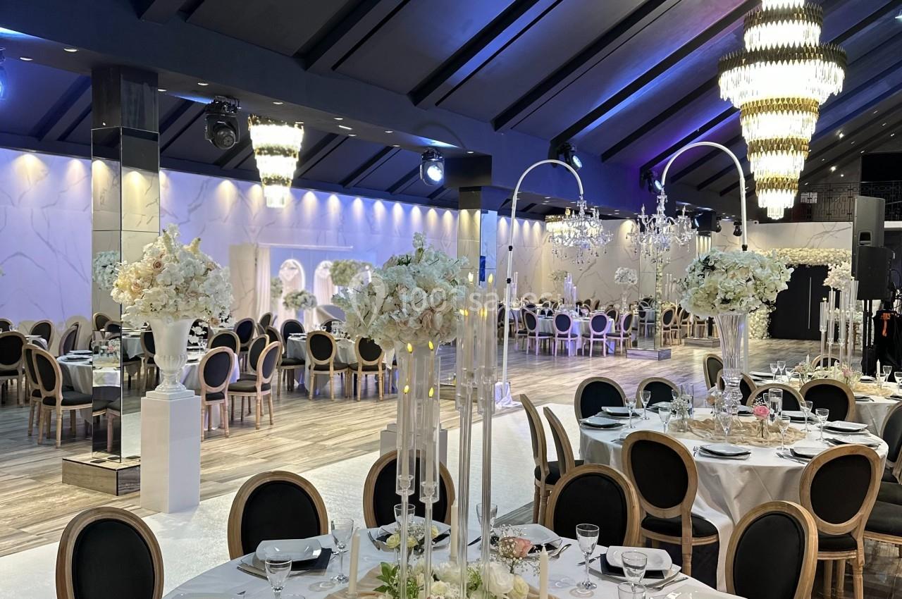 Salle de réception élégante avec tables dressées, décor floral blanc et lustres imposants sous un plafond voûté.