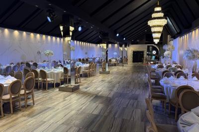 Salle de réception élégante avec tables rondes dressées, chaises transparentes et lustres suspendus.