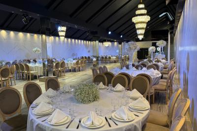Salle de réception élégante avec tables rondes dressées, chaises transparentes et lustres suspendus.