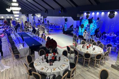 Salle de réception élégante avec tables rondes dressées, chaises transparentes et lustres suspendus.