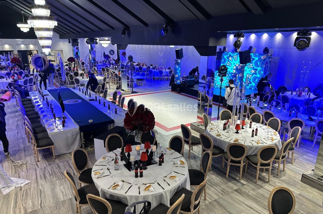 Salle de réception décorée avec des tables rondes, une piste de danse centrale et un éclairage lumineux.