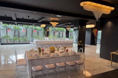 Salle de réception élégante avec tables rondes dressées, chaises transparentes et lustres suspendus.