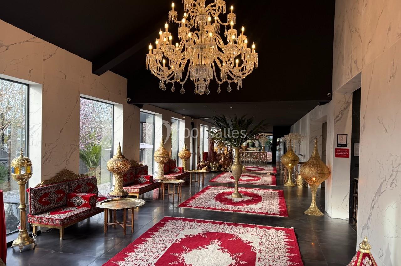 Intérieur élégant avec lustre imposant, tapis rouges ornés et mobilier doré dans un espace lumineux et raffiné.