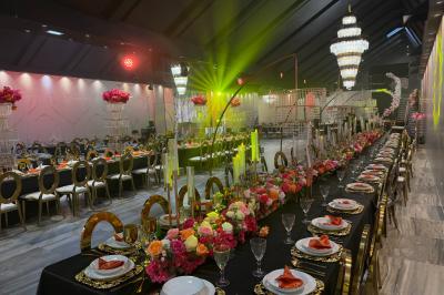 Salle de réception élégante avec tables rondes dressées, chaises transparentes et lustres suspendus.