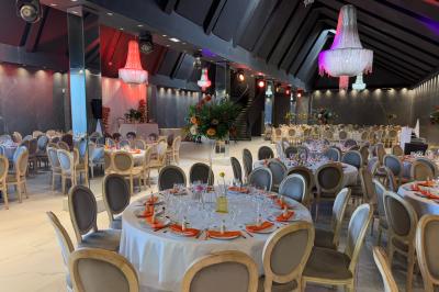 Salle de réception élégante avec tables rondes dressées, chaises transparentes et lustres suspendus.