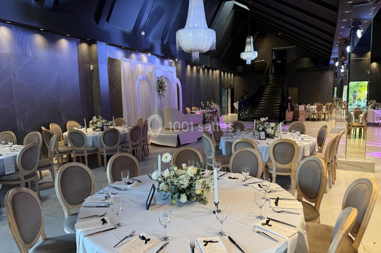 Salle de réception élégante avec tables rondes dressées, chandeliers suspendus et décor floral raffiné.