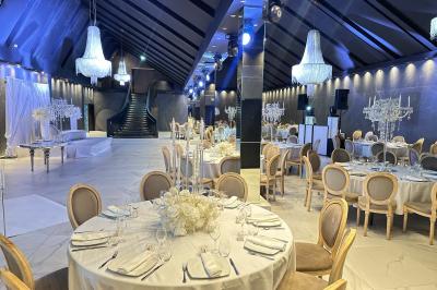 Salle de réception élégante avec tables rondes dressées, chaises transparentes et lustres suspendus.