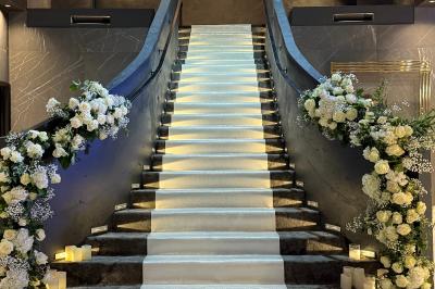 Salle de réception élégante avec tables rondes dressées, chaises transparentes et lustres suspendus.