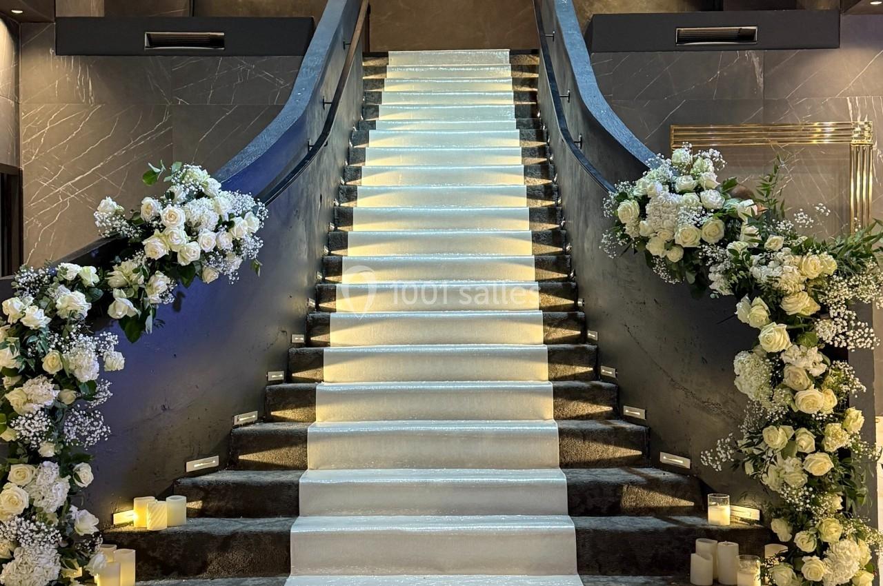 Escalier central élégant avec rampe noire, décoré de fleurs blanches et éclairé par des lumières tamisées.