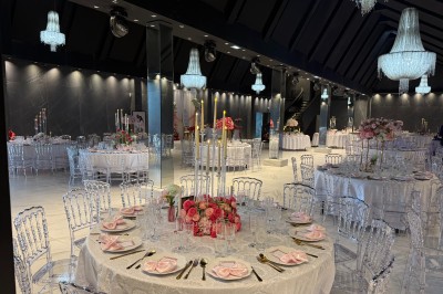 Salle de réception élégante avec tables rondes dressées, chaises transparentes et lustres suspendus.