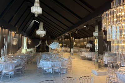 Salle de réception élégante avec tables rondes dressées, chaises transparentes et lustres suspendus.