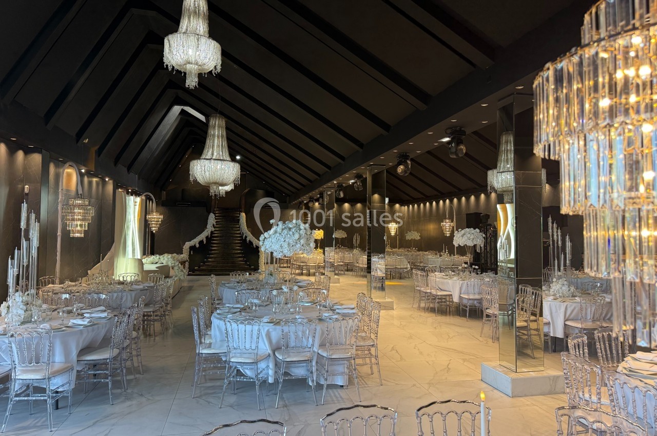 Salle de réception élégante avec tables dressées, chaises transparentes et lustres en cristal suspendus.