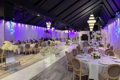 Salle de réception élégante avec tables rondes dressées, chaises transparentes et lustres suspendus.