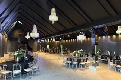 Salle de réception élégante avec tables rondes dressées, chaises transparentes et lustres suspendus.