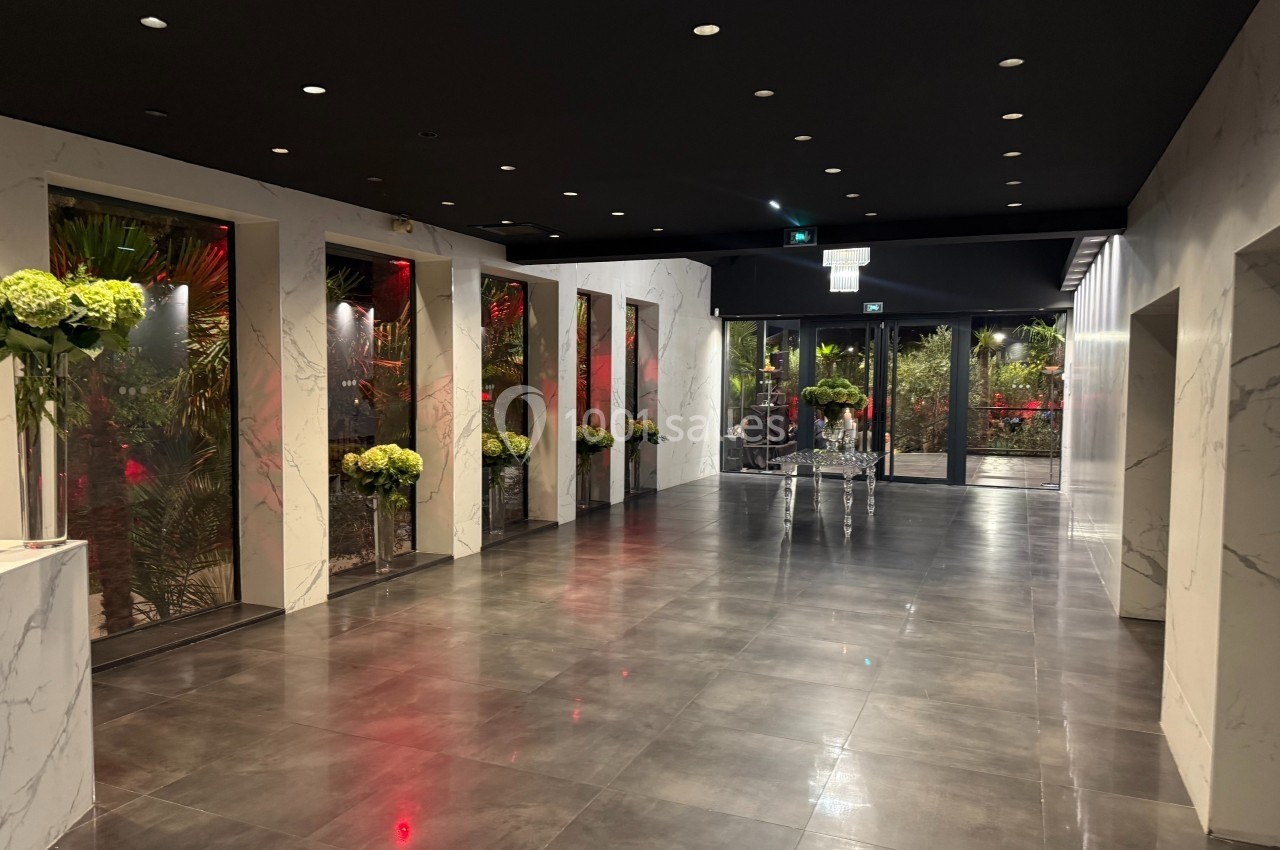 Couloir moderne avec sol en carrelage sombre, murs effet marbre, éclairage tamisé et décorations florales.