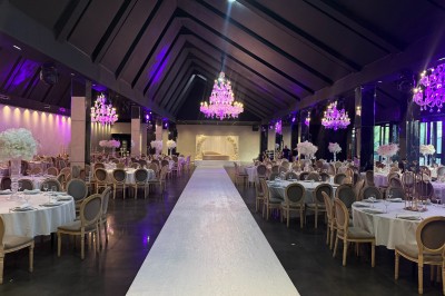 Salle de réception élégante avec tables rondes dressées, chaises transparentes et lustres suspendus.