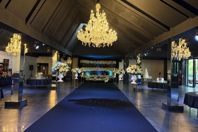 Salle de réception élégante avec tables rondes dressées, chaises transparentes et lustres suspendus.
