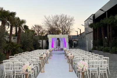 Salle de réception élégante avec tables rondes dressées, chaises transparentes et lustres suspendus.