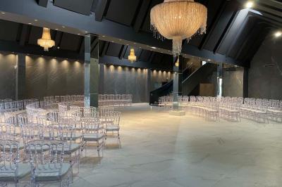 Salle de réception élégante avec tables rondes dressées, chaises transparentes et lustres suspendus.