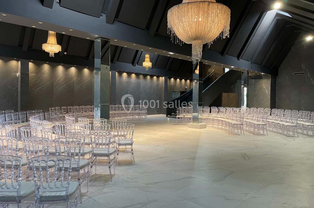 Salle de réception moderne avec chaises transparentes disposées en rangées et lustres en cristal suspendus.