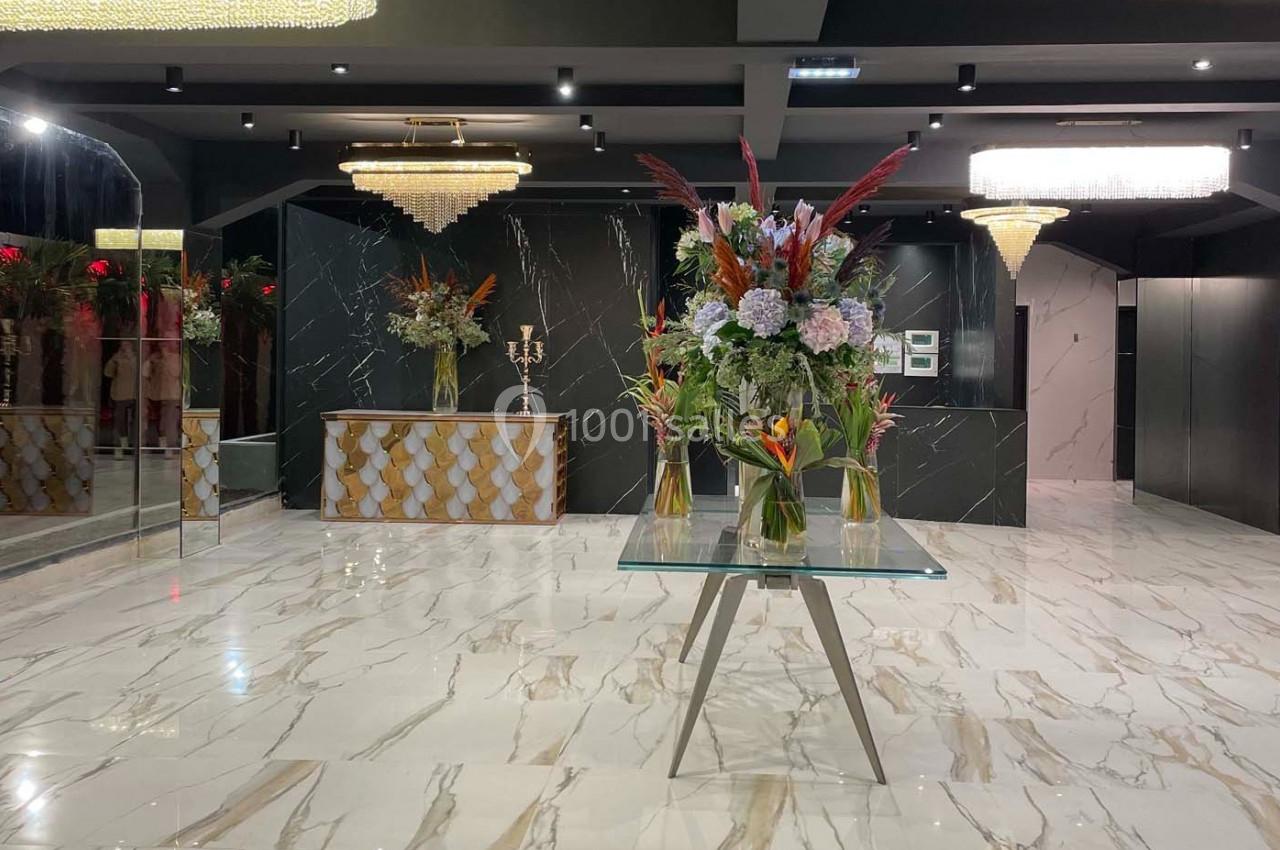 Hall élégant avec sol en marbre, comptoir décoratif, lustres et table centrale ornée de grands bouquets de fleurs.