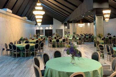 Salle de réception élégante avec tables rondes noires, chaises transparentes, lustres en cristal et décorations végétales.