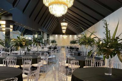 Salle de réception élégante avec tables rondes noires, chaises transparentes, lustres en cristal et décorations végétales.