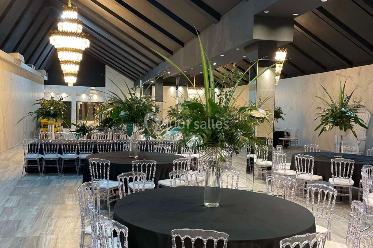 Salle de réception élégante avec tables rondes dressées de nappes noires et centres de table composés de plantes vertes.