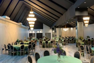 Salle de réception élégante avec tables rondes noires, chaises transparentes, lustres en cristal et décorations végétales.