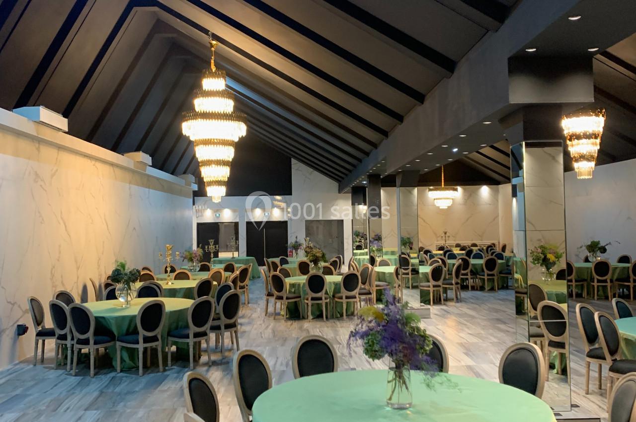 Salle de réception élégante avec tables rondes couvertes de nappes vertes, chaises noires et lustres imposants.