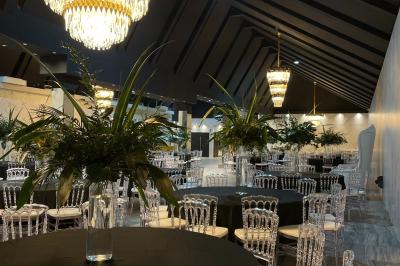 Salle de réception élégante avec tables rondes noires, chaises transparentes, lustres en cristal et décorations végétales.