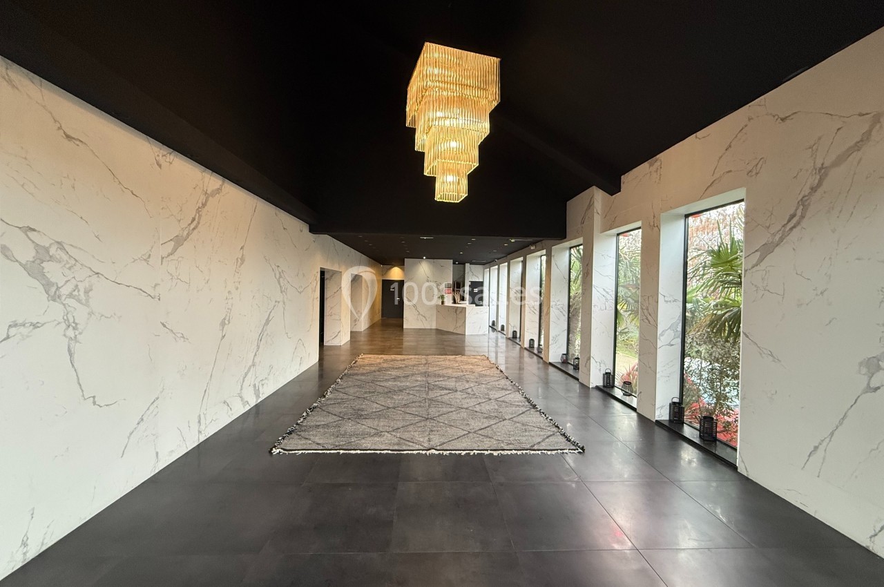 Hall moderne avec murs effet marbre, sol sombre, tapis géométrique et lustres suspendus en cascade.