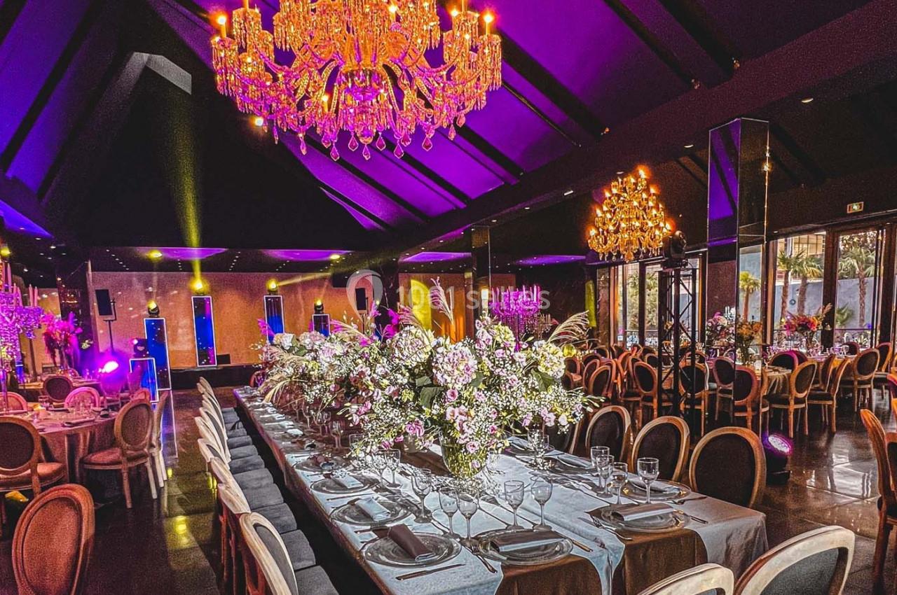 Salle de réception élégante avec tables décorées de fleurs, chaises disposées et lustres illuminant l'espace.