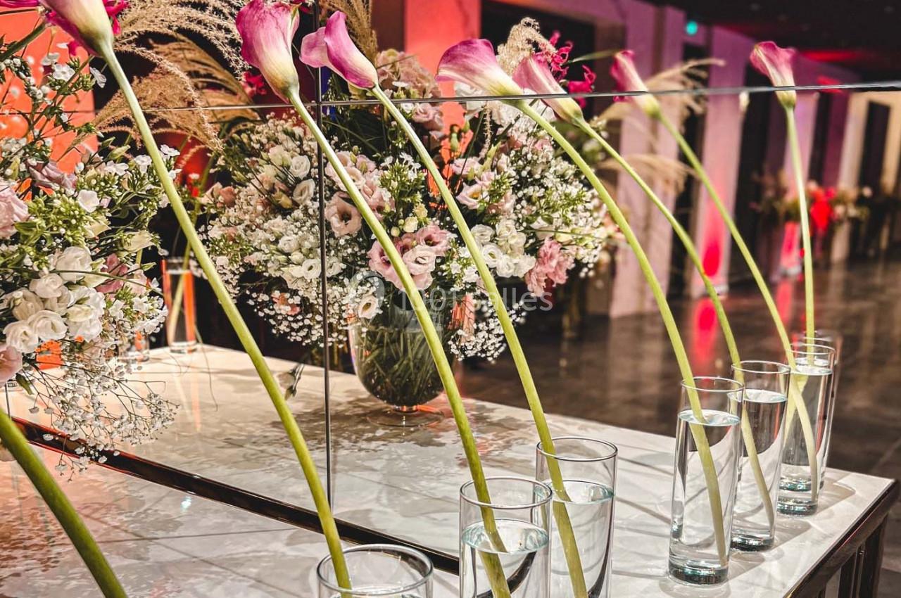 Fleurs roses et blanches disposées dans des vases en verre devant un miroir reflétant un décor floral.