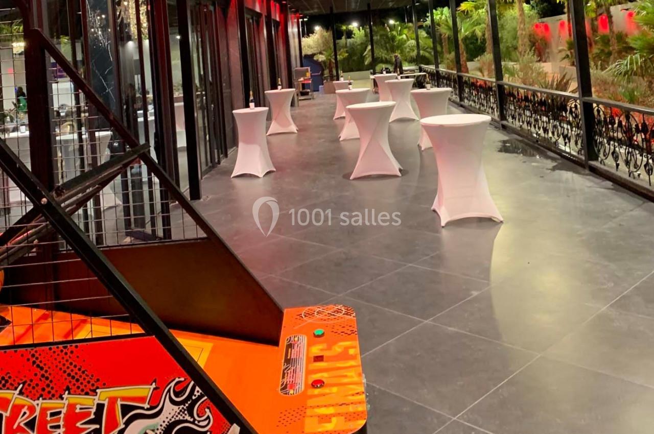 Salle lumineuse avec grandes baies vitrées, tables hautes blanches et vue sur un jardin verdoyant.